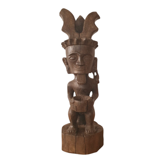 Statue Batak en bois de Sumatra représentant un personnage accroupi tenant un récipient, coiffé de deux ailes stylisées – H54 cm.